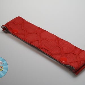 May include: Red fabric headband with a heart pattern and two red buttons. The headband is folded in half.