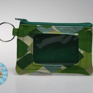 May include: Green and white patterned ID holder with a clear window and a silver key ring. The ID holder has a zipper closure and a geometric design. The product is a small, rectangular wallet.