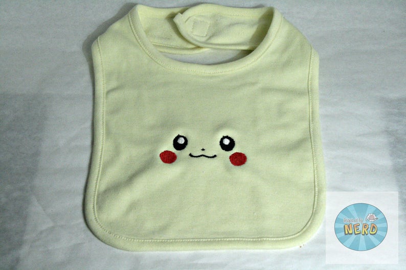 K&ouml;nnte beinhalten: Ein hellgelber Baby-L&auml;tzchen mit einem gestickten Pikachu-Gesicht. Das Gesicht hat schwarze Augen, eine rote Nase und ein kleines L&auml;cheln.
