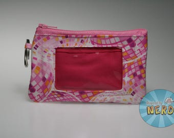Peut inclure: Porte-monnaie à motif rose et blanc avec une fenêtre transparente et une fermeture éclair rose. Le sac a un porte-clés argenté attaché sur le côté. Le motif est une mosaïque de carrés roses, jaunes et violets.