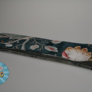 May include: A teal blue headband with a floral pattern featuring pink, white, and yellow flowers. The headband is made of a soft, velvety fabric.