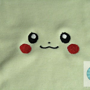K&ouml;nnte beinhalten: Ein hellgr&uuml;ner Stoff mit einem gestickten Pikachu-Gesicht. Das Gesicht hat schwarze Augen mit wei&szlig;en Highlights, eine schwarze Nase und einen schwarzen l&auml;chelnden Mund. Die Wangen sind rot.