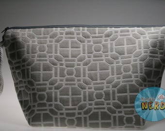 Pode incluir: Uma bolsa cinza com zíper e um padrão geométrico. A bolsa tem uma alça de corda cinza claro e um zíper cinza escuro. O padrão geométrico é um tom de cinza mais claro e cobre toda a superfície.