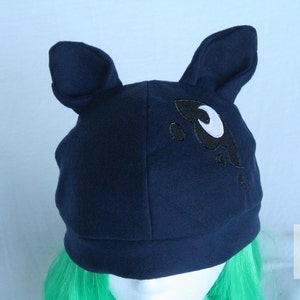 May include: A navy blue beanie with a black and white crescent moon design. The beanie has two floppy ears.