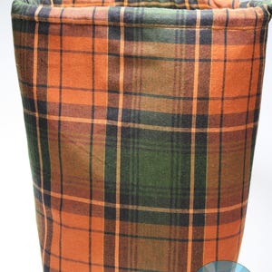 May include: A fabric storage basket with a plaid pattern in orange, green, and black. The basket has a cylindrical shape and a drawstring closure at the top. The design is inspired by a nerd theme.