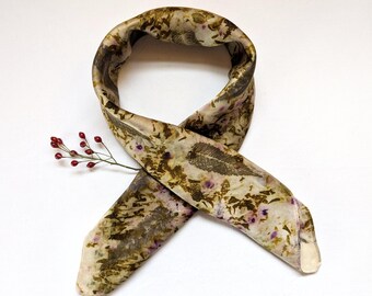 May include: A silk scarf with a botanical print in shades of green, brown, and purple. The scarf is tied in a knot and has a raw edge.