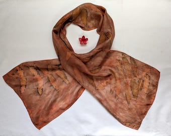 May include: A brown silk scarf with a leaf pattern. The scarf is folded in half and laid flat on a white surface.