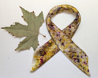 May include: A white silk scarf with a floral pattern in shades of yellow, purple, and brown. The scarf is tied in a knot and the ends are hanging down.