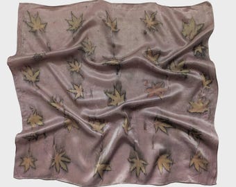 May include: A mauve-colored silk scarf with a repeating pattern of maple leaves in shades of yellow, orange, and black. The scarf has a soft, flowing texture and is slightly wrinkled, suggesting it has been worn or handled.