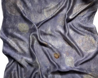 May include: A draped, silk scarf in shades of blue and gray, with a subtle sheen. The fabric is adorned with a pattern of leaf-like imprints in muted tones of beige and brown. The scarf's folds create shadows, enhancing the texture and depth of the design.