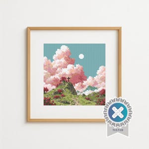 Op de afbeelding: Een ingelijste kruissteeklandschap met een groene heuvel met een kruis, roze wolken en een volle maan tegen een blauwgroene lucht. Het kunstwerk zit in een houten lijst en heeft een "TESTED" zegel.