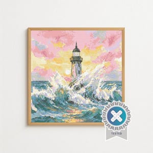 May include: A square cross-stitch pattern featuring a lighthouse surrounded by crashing ocean waves under a sunset sky with pink and yellow clouds. The design is framed in a light wood border and includes a circular badge with the text TESTED.