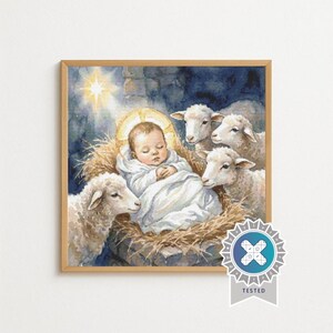 May include: A square framed artwork depicting a baby wrapped in white cloth lying in a bed of straw, surrounded by three white sheep. A bright star shines in the dark blue background above the baby. A circular badge with the word TESTED is visible.