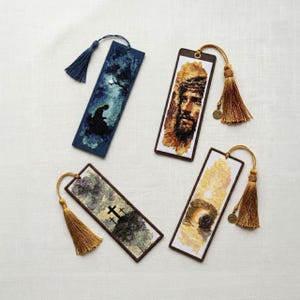 Puede incluir: Cuatro marcadores bordados con temas religiosos. Uno representa una figura en un paisaje oscuro, otro un retrato de Jesús, y otros dos presentan cruces y una tumba. Cada marcador tiene una borla.