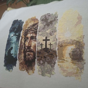 Puede incluir: Una pieza rectangular de tela color hueso con un diseño de bordado en punto de cruz que presenta cuatro paneles verticales. Los paneles muestran una silueta en oración, un retrato de Jesús con corona de espinas, tres cruces y una tumba.