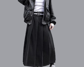 Può includere: Una persona indossa una giacca di pelle nera sopra una camicia bianca, una gonna a pieghe nera e scarpe da ginnastica bianche. La giacca ha più tasche e una cintura a doppia fibbia. L'outfit è un mix di trame e stili.