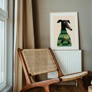 May include: A framed art print featuring a stylized illustration of a black dog wearing a green and black striped sweater, holding a green mug. The dog has long ears and a long snout. The background is a neutral beige color.