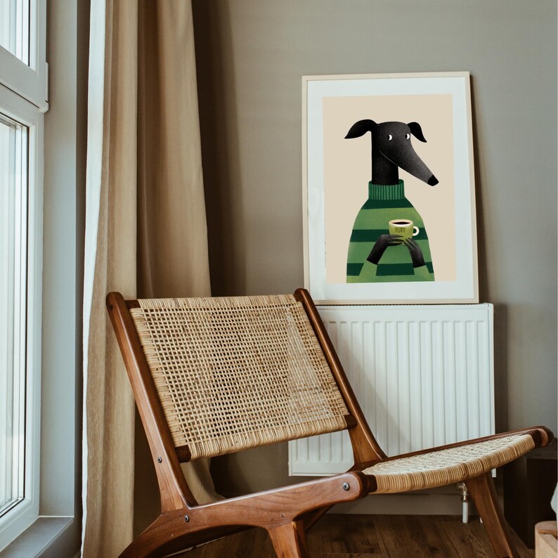 May include: A framed art print featuring a stylized illustration of a black dog wearing a green and black striped sweater, holding a green mug. The dog has long ears and a long snout. The background is a neutral beige color.