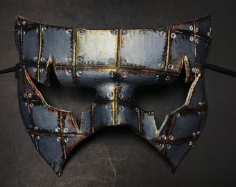 May include: A silver and gold steampunk-style masquerade mask with a geometric design. The mask has a raised, textured surface and is made of leather.