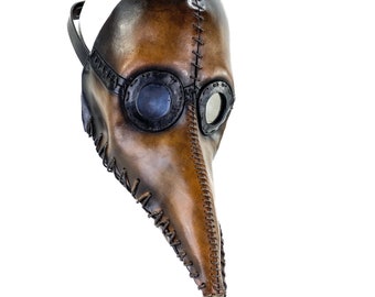 May include: A brown leather plague doctor mask with a long, beak-like nose and stitched seams. The mask features circular, dark-rimmed eye lenses and a strap for securing it to the head. The mask is designed with a vintage aesthetic.