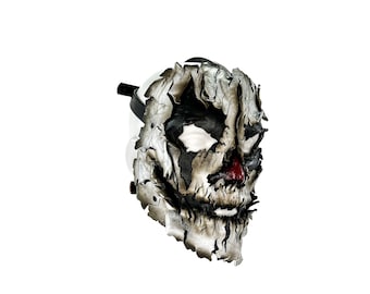 May include: A white and black leather mask with a cracked and weathered appearance. The mask has a red nose and a wide, toothy grin.