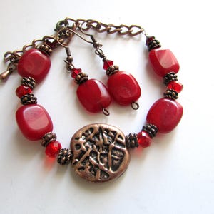 May include: A red and copper bracelet and earrings set with red gemstone beads and a copper charm.