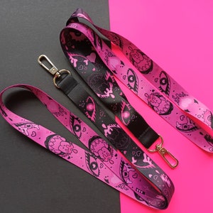 May include: Two pink and black patterned lanyards with silver clasps. The lanyards feature a repeating design of eyes, hearts, and dripping teeth.