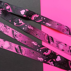 May include: Three pink and black patterned ribbon lanyards with a gradient background and black and white eye and heart designs. The text "Sugar Daddy" is printed on one of the lanyards.