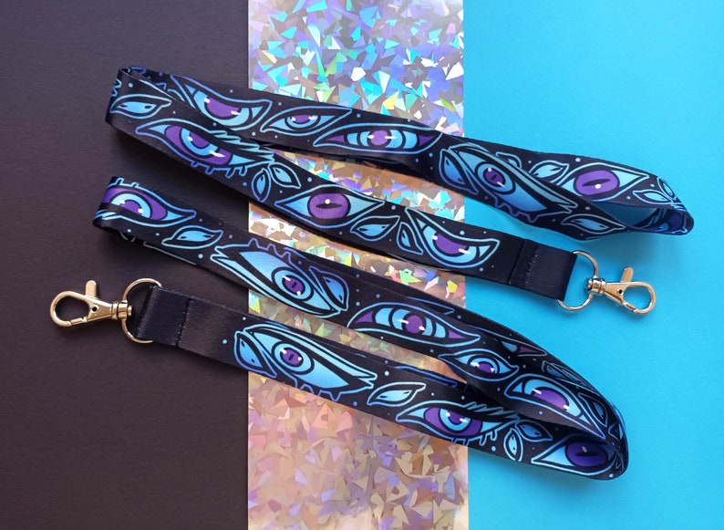 May include: Two black lanyards with blue and purple eye designs. The lanyards have silver swivel clips.