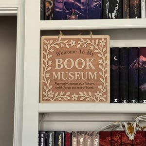 "Book Museum" sign neatly displayed on a white bookshelf, surrounded by fantasy books, adding a whimsical touch to a personal library.