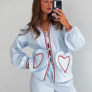 Puede incluir: Conjunto de pijama de cuadros vichy azul claro y blanco con ribete rojo. La parte superior presenta bolsillos en forma de coraz&oacute;n y un frente con lazo. El conjunto est&aacute; hecho de un material suave y c&oacute;modo.