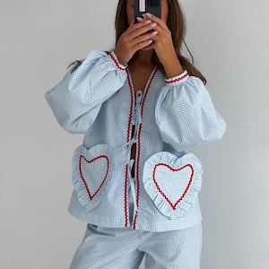 Puede incluir: Conjunto de pijama de cuadros vichy azul claro y blanco. La parte superior tiene bolsillos en forma de coraz&oacute;n con ribete rojo y bordes con volantes. La chaqueta y los pantalones tienen ribete rojo. Las mangas son abullonadas y la chaqueta tiene cierre de lazo.