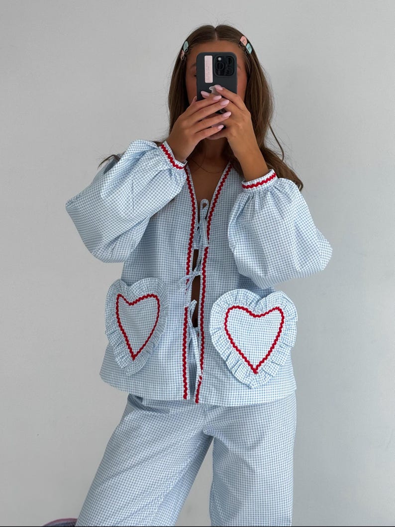 Puede incluir: Conjunto de pijama de cuadros vichy azul claro y blanco. La parte superior tiene bolsillos en forma de coraz&oacute;n con ribete rojo y bordes con volantes. La chaqueta y los pantalones tienen ribete rojo. Las mangas son abullonadas y la chaqueta tiene cierre de lazo.