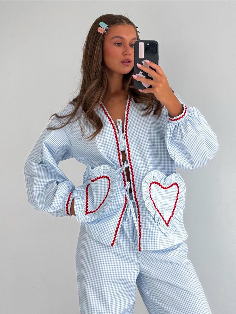 Puede incluir: Conjunto de pijama de cuadros vichy azul claro y blanco con ribete rojo. La parte superior presenta bolsillos en forma de coraz&oacute;n y un frente con lazo. El conjunto est&aacute; hecho de un material suave y c&oacute;modo.