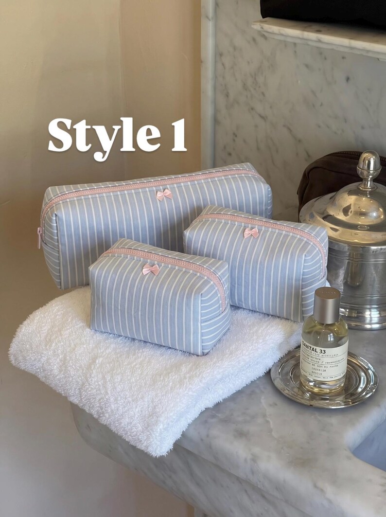 May include: Three light blue and white striped cosmetic bags of varying sizes, each featuring a pale pink zip closure and a small pink bow detail. The text "Style 1" is visible in the upper left corner of the image.