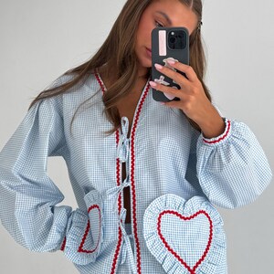 Puede incluir: Conjunto de pijama de cuadros vichy azul claro y blanco con ribete rojo. La parte superior tiene cuello en V, cierre de lazo y bolsillos en forma de coraz&oacute;n. Las mangas son largas y abullonadas. El conjunto est&aacute; hecho de un material suave y c&oacute;modo.