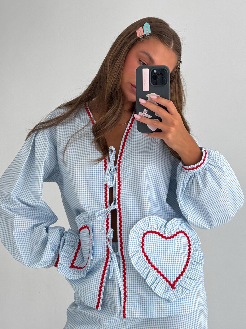 Puede incluir: Conjunto de pijama de cuadros vichy azul claro y blanco con ribete rojo. La parte superior tiene cuello en V, cierre de lazo y bolsillos en forma de coraz&oacute;n. Las mangas son largas y abullonadas. El conjunto est&aacute; hecho de un material suave y c&oacute;modo.