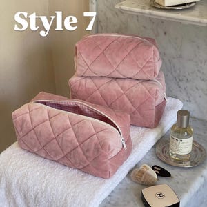 May include: Three dusty pink quilted velvet cosmetic bags with white zippers and a pink and white gingham interior lining. The text "Style 7" is visible in the upper left corner. The bags are rectangular with a soft, plush texture.