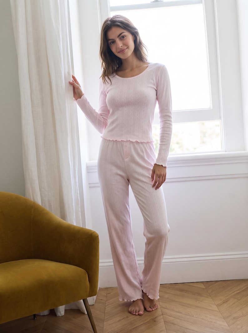 May include: A light pink long-sleeve pajama set featuring a ribbed texture. The top has a scoop neckline and lettuce-edge trim on the cuffs and hem. The matching pants have a straight-leg fit with a button-front detail at the waist and a lettuce-edge hem.