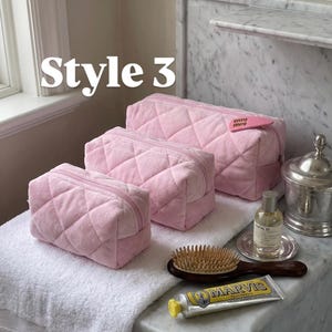 May include: Three light pink quilted cosmetic bags of varying sizes, each featuring a zipper closure. The largest bag has a small pink heart-shaped tag attached. The text "Style 3" is visible in the upper left corner of the image.