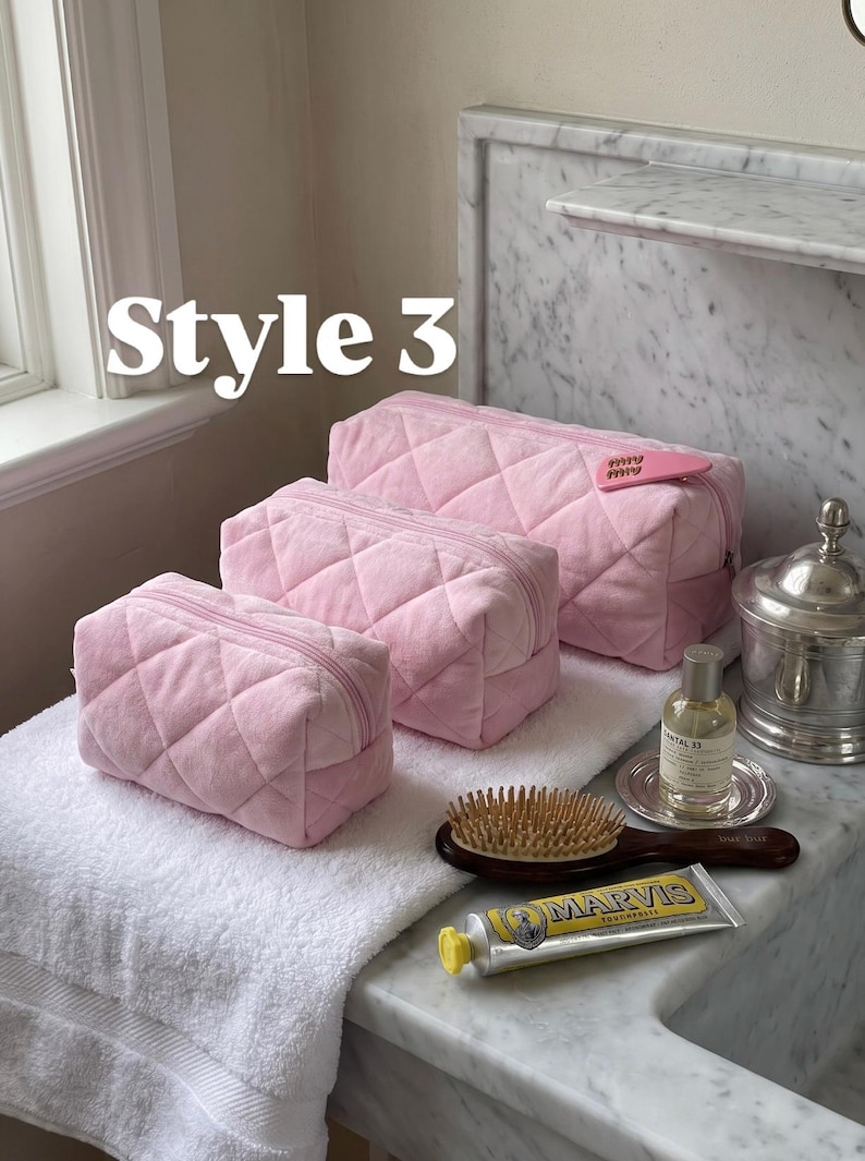May include: Three light pink quilted cosmetic bags of varying sizes, each featuring a zipper closure. The largest bag has a small pink heart-shaped tag attached. The text "Style 3" is visible in the upper left corner of the image.