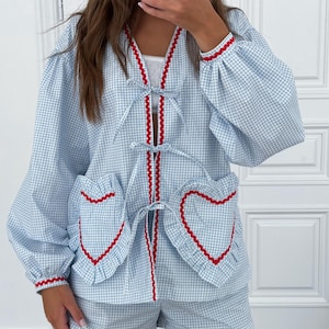 Puede incluir: Conjunto de pijama de cuadros vichy azul claro y blanco. El conjunto incluye una parte superior de manga larga con ribete rojo y bolsillos en forma de coraz&oacute;n, y pantalones cortos a juego. La parte superior tiene cuello en V y lazos.