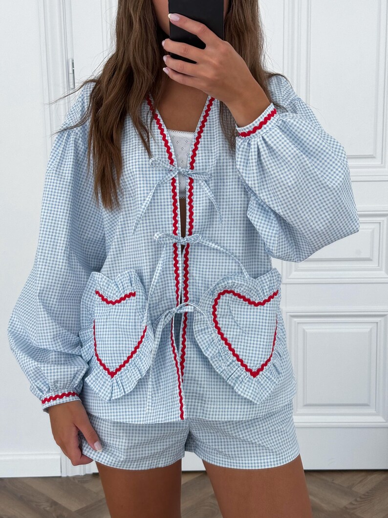 Puede incluir: Conjunto de pijama de cuadros vichy azul claro y blanco. El conjunto incluye una parte superior de manga larga con ribete rojo y bolsillos en forma de coraz&oacute;n, y pantalones cortos a juego. La parte superior tiene cuello en V y lazos.
