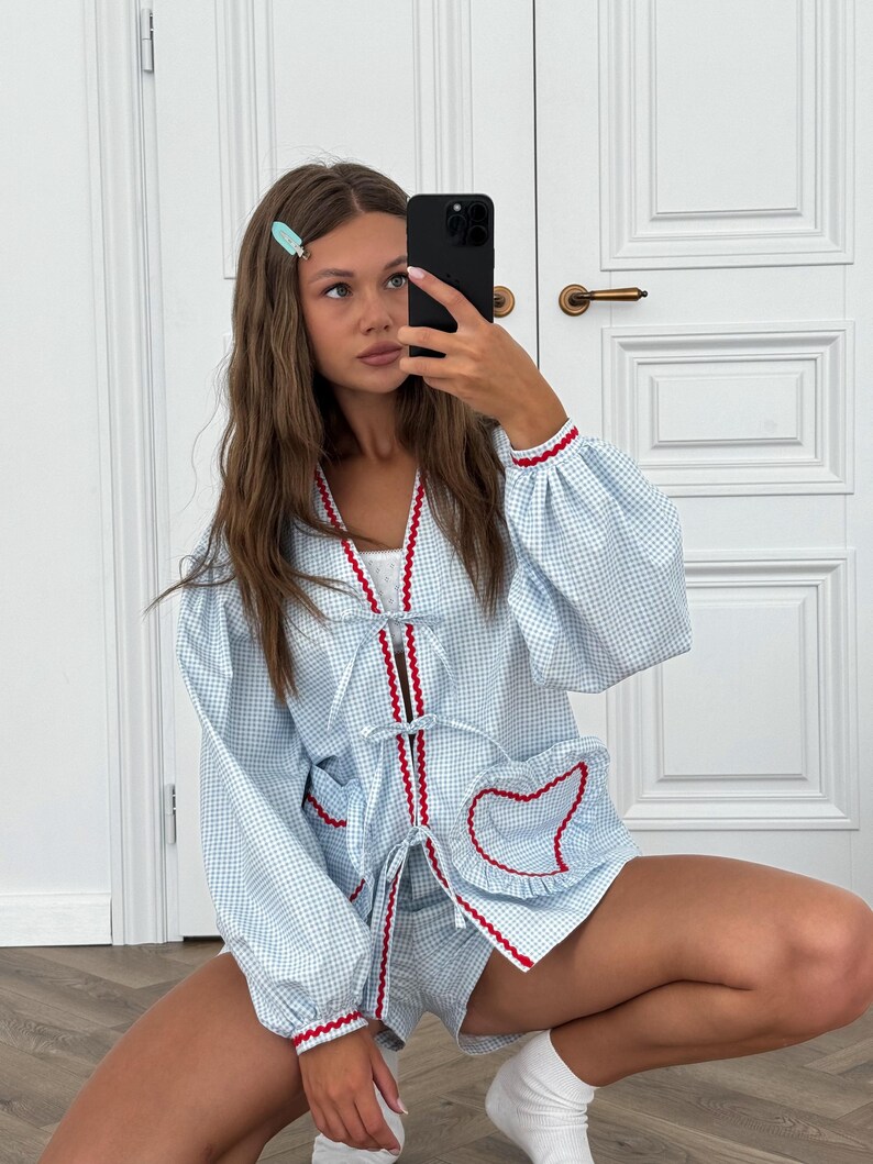 Puede incluir: Conjunto de pijama de cuadros vichy azul claro con ribete rojo. El conjunto incluye una parte superior de manga larga con cierre de lazo y bolsillo en forma de coraz&oacute;n, y pantalones cortos a juego. Los pu&ntilde;os y los bordes est&aacute;n ribeteados en rojo.