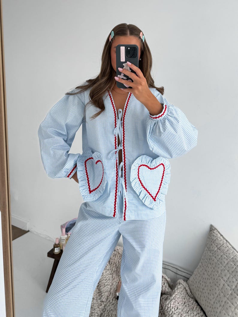 Puede incluir: Conjunto de pijama de cuadros vichy azul claro y blanco. La parte superior tiene cuello en V con ribete rojo y bolsillos en forma de coraz&oacute;n con ribete rojo. La parte superior de manga larga y los pantalones tienen un ajuste holgado.