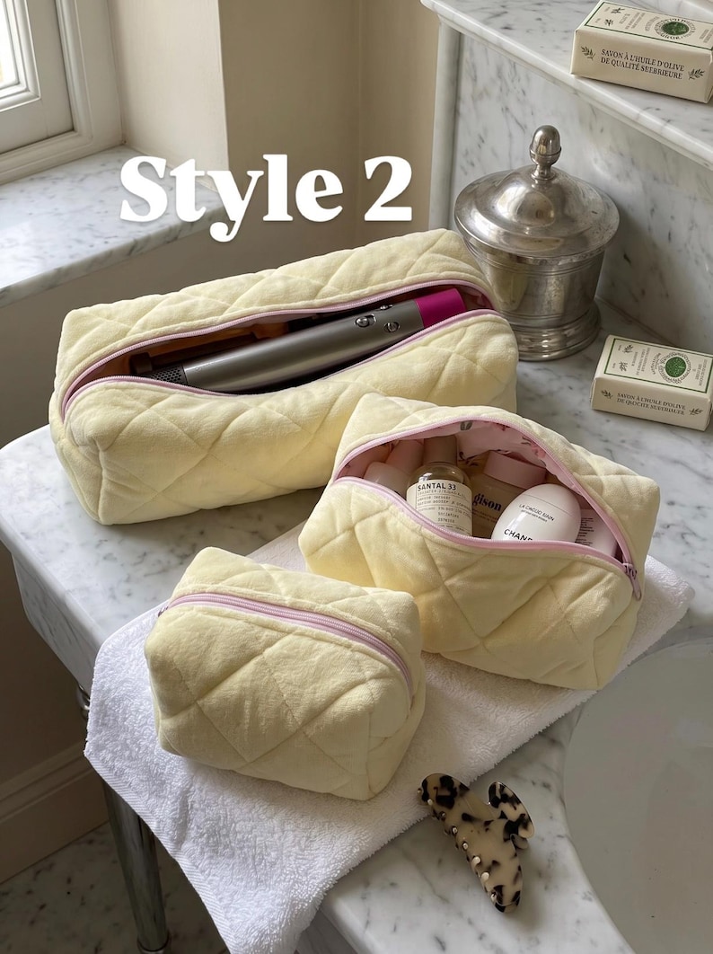 May include: Three pale yellow quilted pouches with soft fabric exteriors and light pink zippers. The largest pouch contains a metallic hair styling tool, the medium pouch holds various skincare bottles, and the smallest pouch is empty.