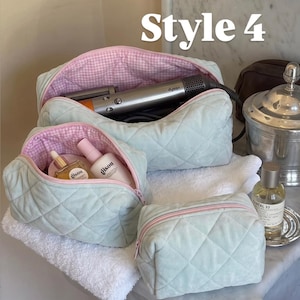 May include: Three quilted sage green cosmetic bags with pink zippers and a pink and white gingham interior lining. The bags are open, revealing a silver hair styling tool and two Gisou brand bottles inside. The text Style 4 appears at the top.