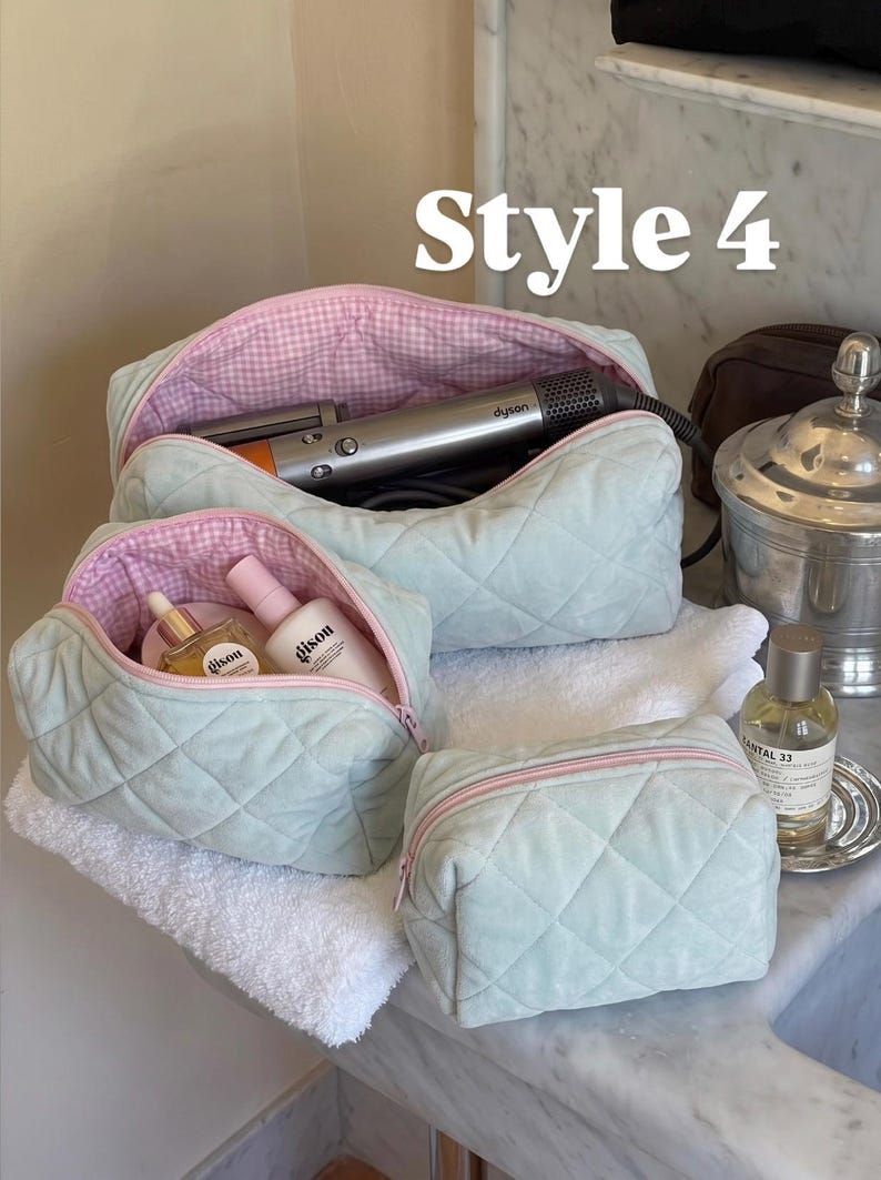 May include: Three quilted sage green cosmetic bags with pink zippers and a pink and white gingham interior lining. The bags are open, revealing a silver hair styling tool and two Gisou brand bottles inside. The text Style 4 appears at the top.