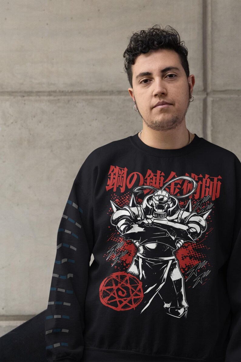 May include: Black sweatshirt featuring a graphic of a character from the anime series Fullmetal Alchemist. The design includes Japanese text and a red alchemic circle. The sleeve has a pattern of blue and gray lines.