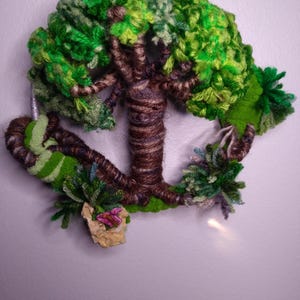 May include: A green, brown, and white yarn tree wall hanging with a butterfly and a rock. The tree is made of yarn and is wrapped around a metal hoop.